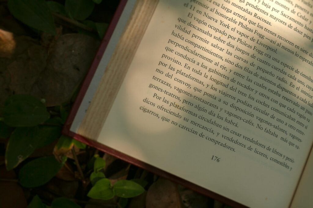 An open book lies on a leafy ground with sunlight illuminating the printed text.